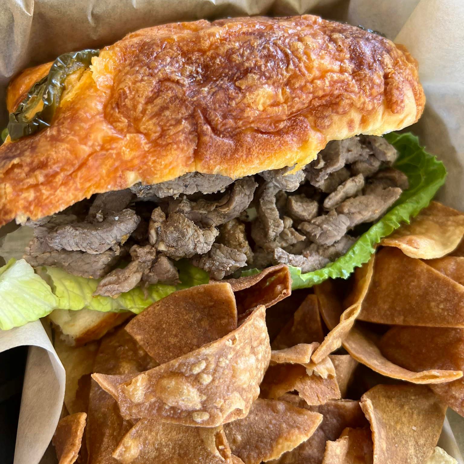 Steak sandwich on toasted bread with lettuce and a side of chips