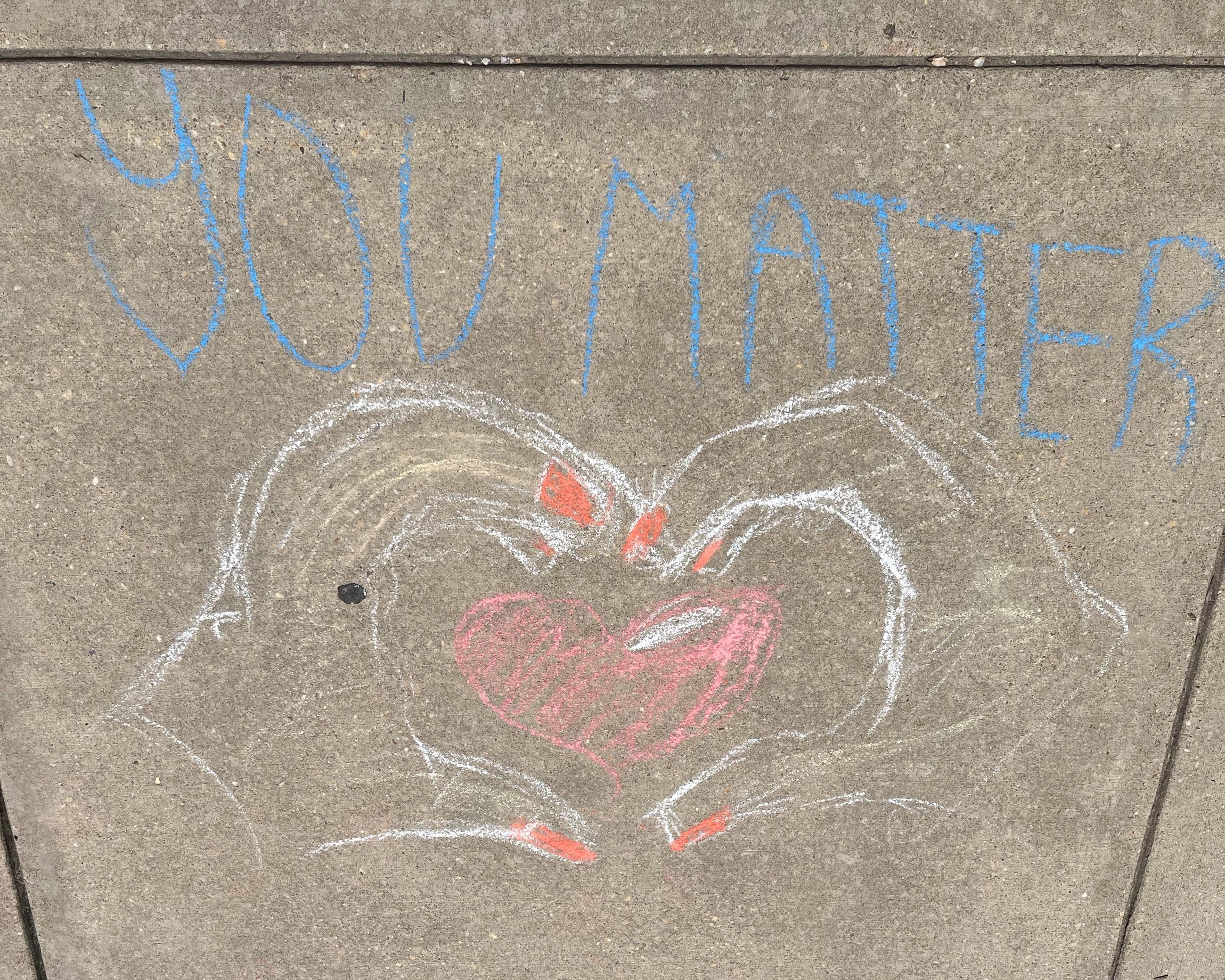 Multicolored chalk art and students near the flagpole in front of Calvert High School.
