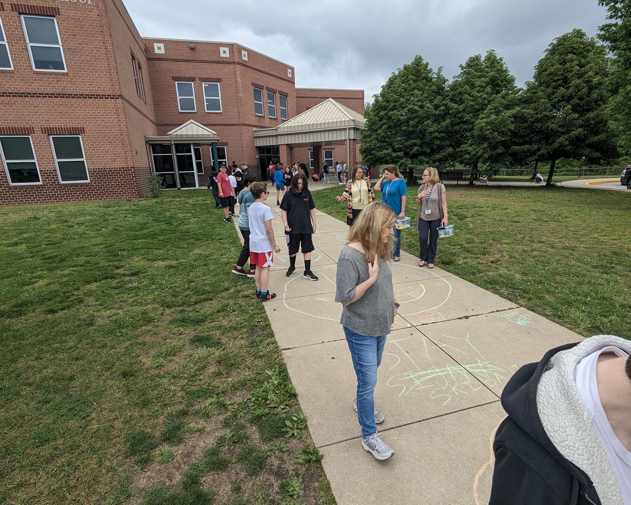 Adults and children looking at chalk art on the sidewalk in front of Windy Hill Middle School.