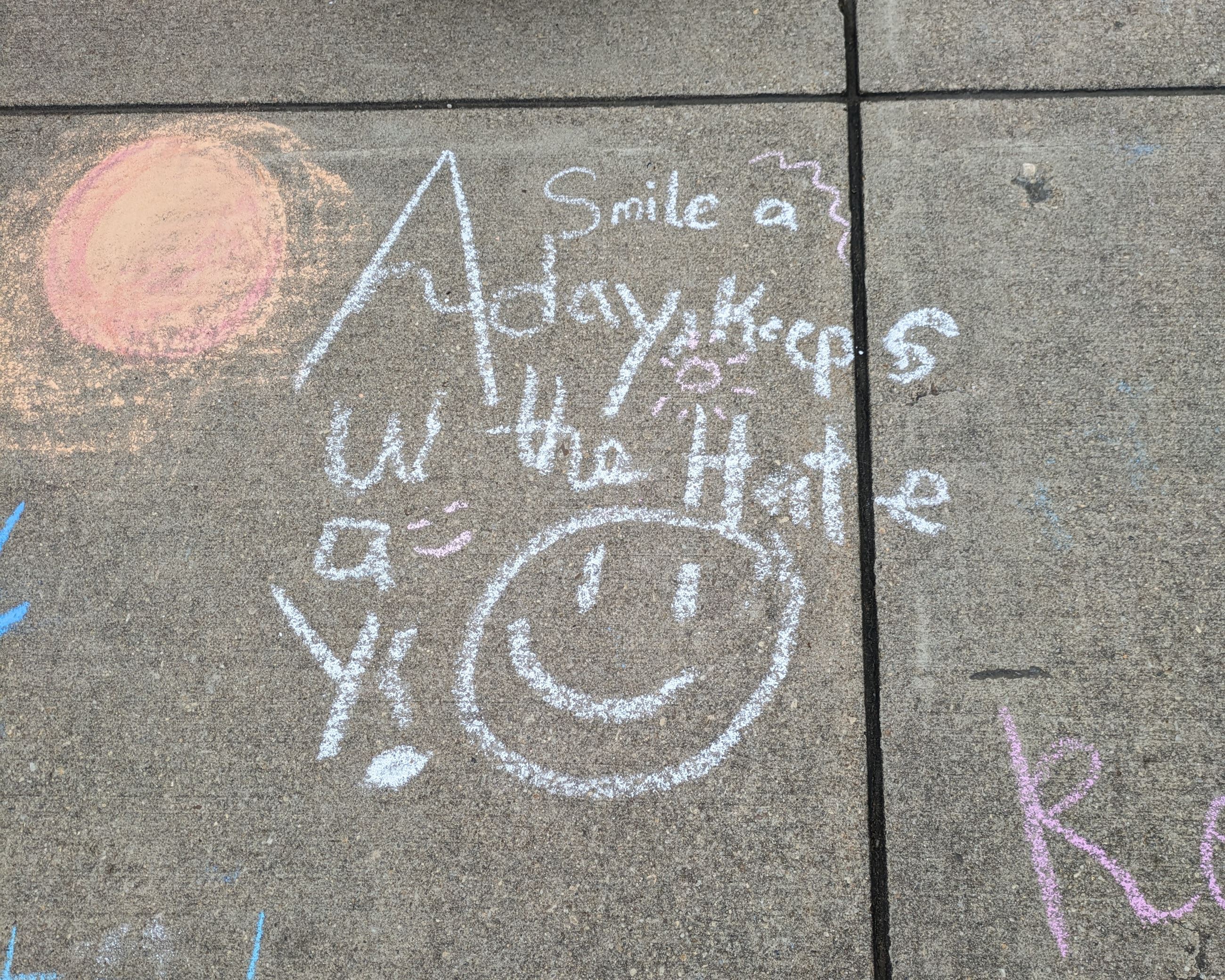 Chalk art of a sun, a smiley face, and text that reads "A smile a day keeps the hate away!"